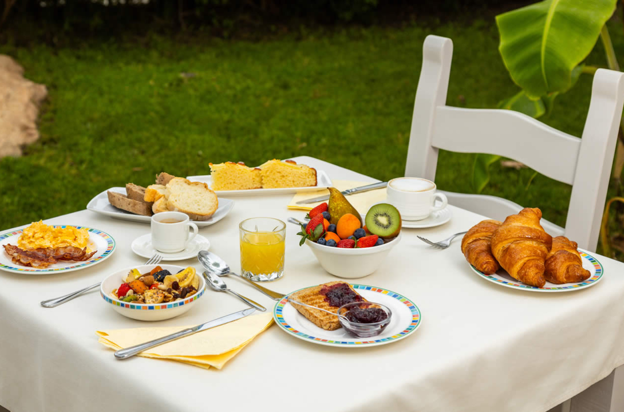 Colazione all'aperto con frutta, croissant, pane, uova e succo d'arancia.