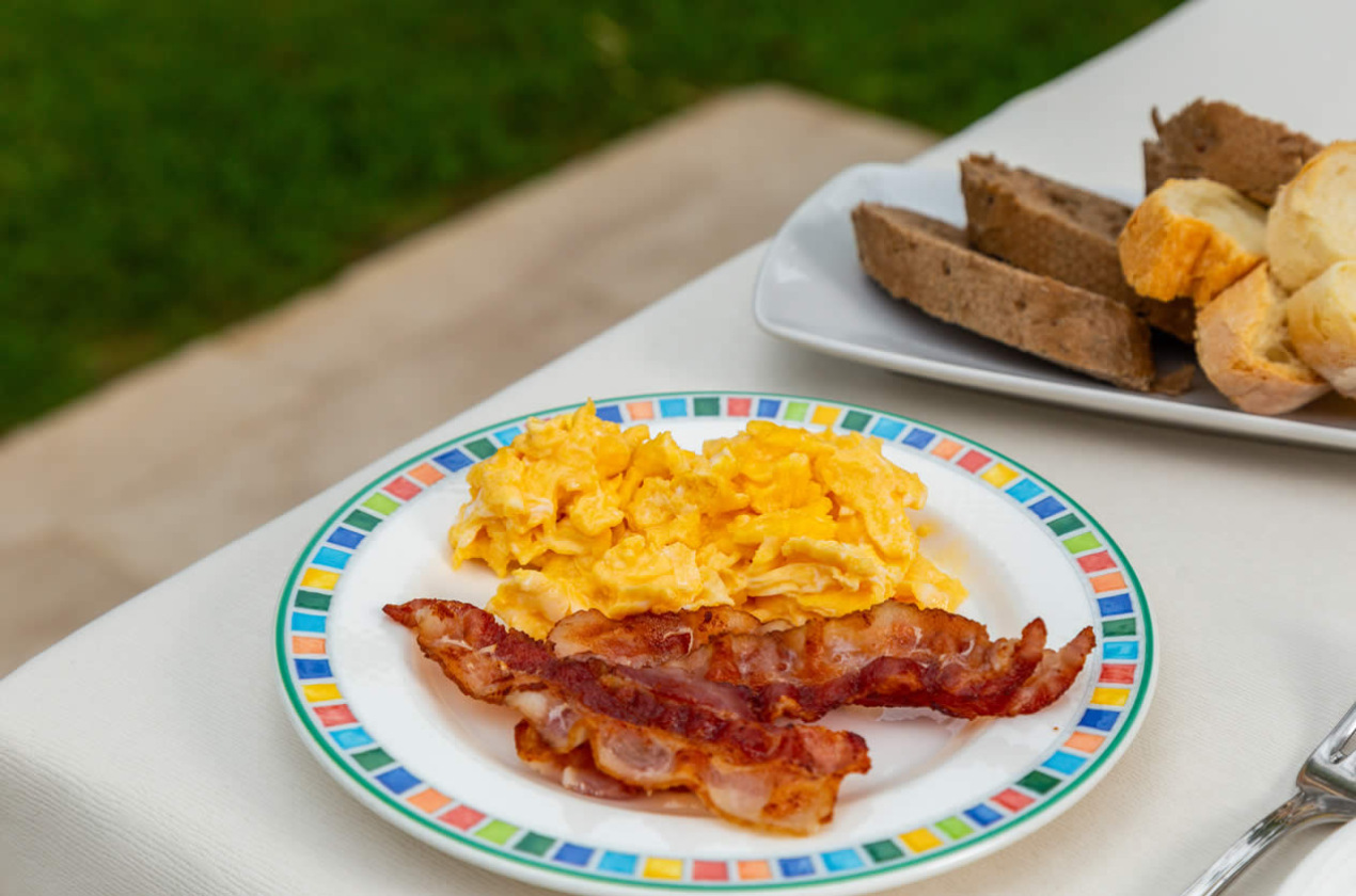 Colazione con uova strapazzate, pancetta croccante e pane assortito su un piatto colorato.