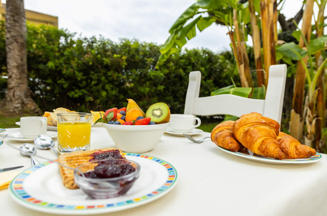 Colazione all'aperto con croissant, frutta fresca, succo d'arancia e marmellata.