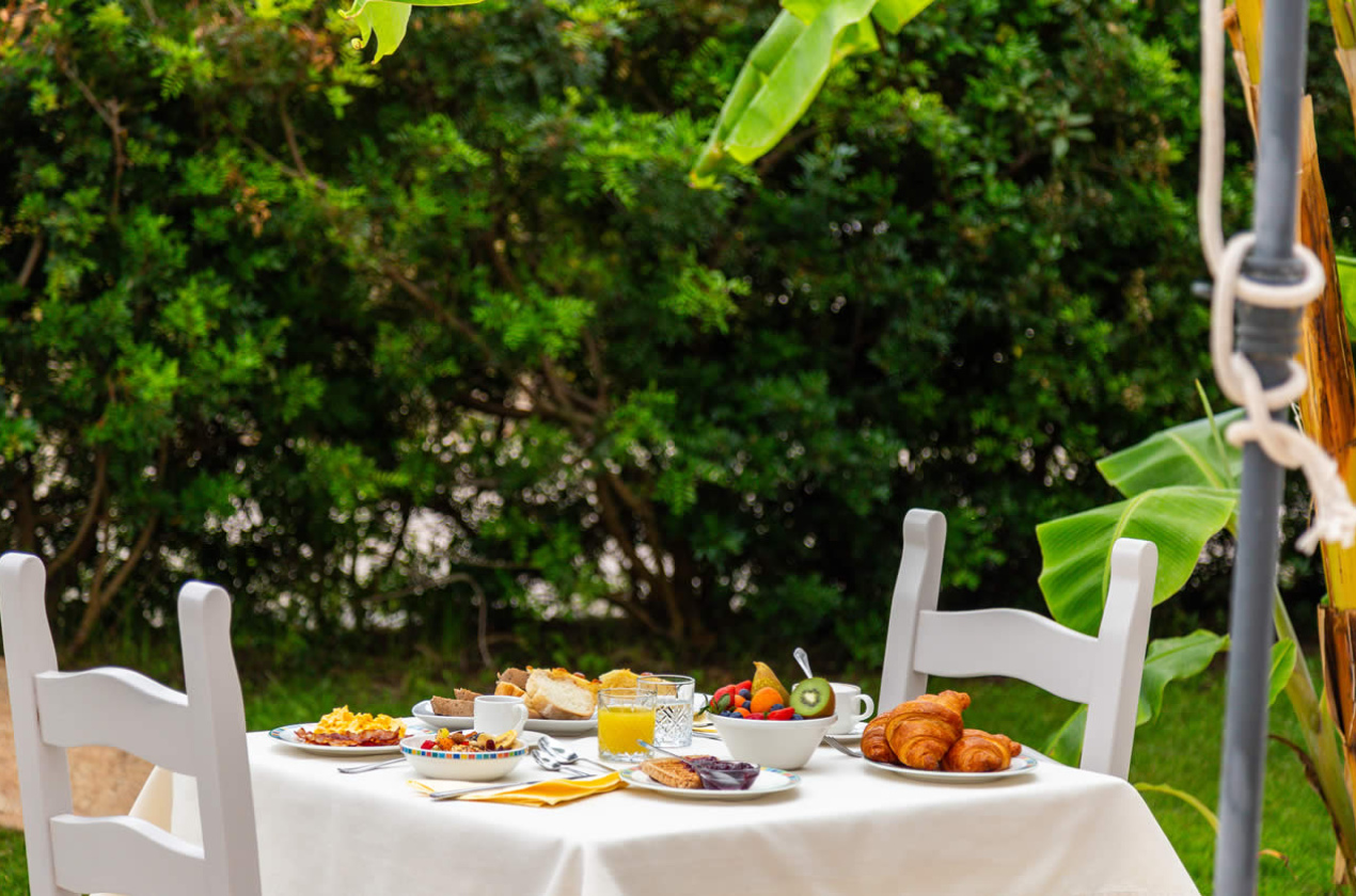 Colazione all'aperto con croissant, frutta, succo d'arancia e pane su tavolo bianco.