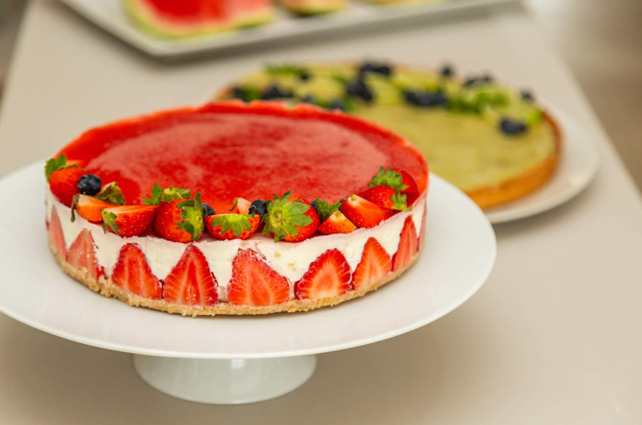 Cheesecake alle fragole con decorazioni di frutta fresca su piatto bianco.