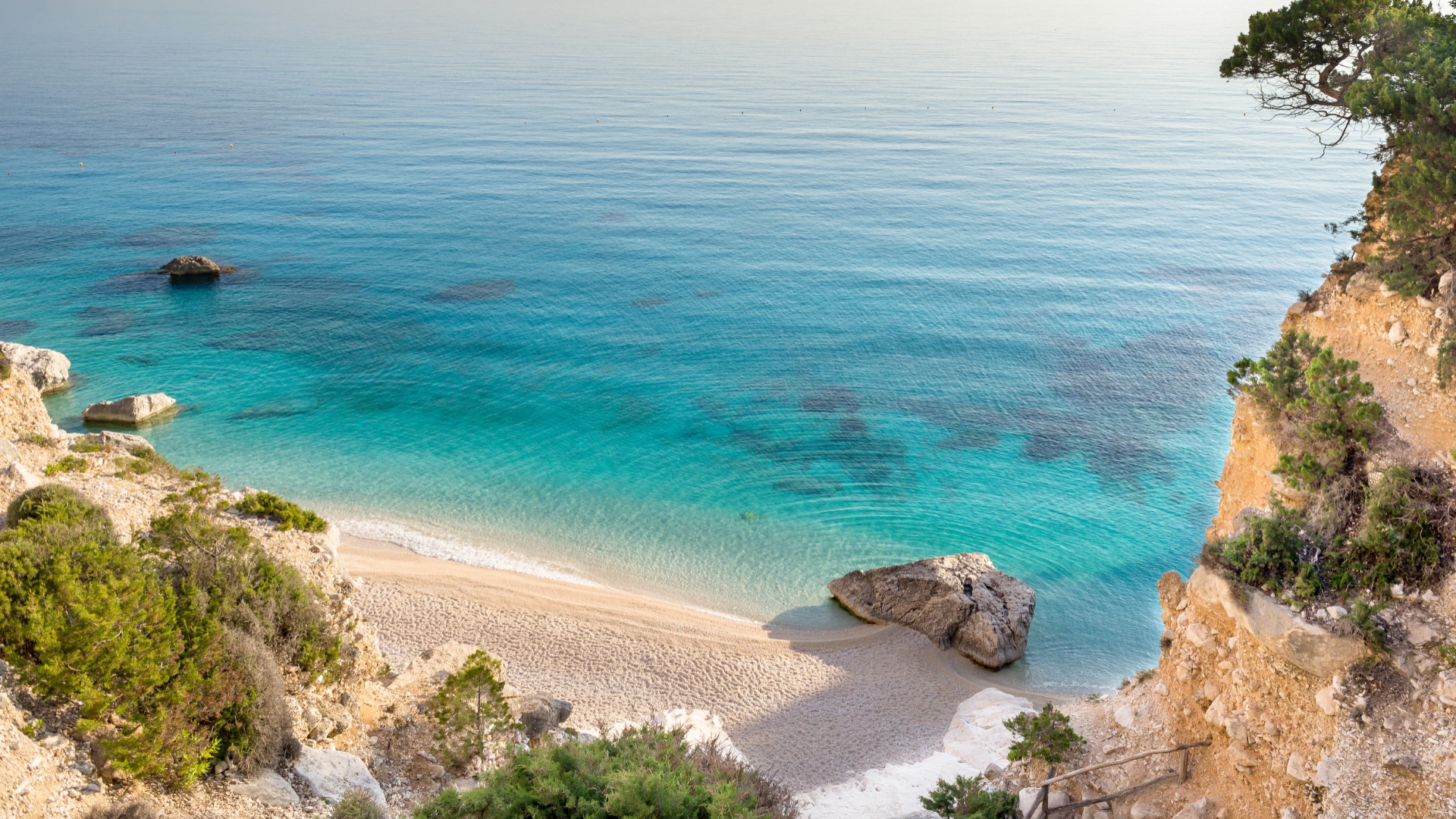 Spiaggia isolata con sabbia chiara, mare turchese e scogli, circondata da scogliere verdi.