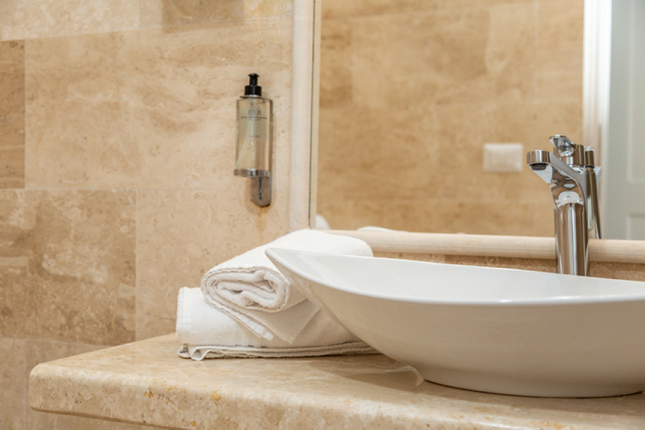 Bagno elegante con lavabo moderno, asciugamani bianchi e dispenser sapone su parete beige.