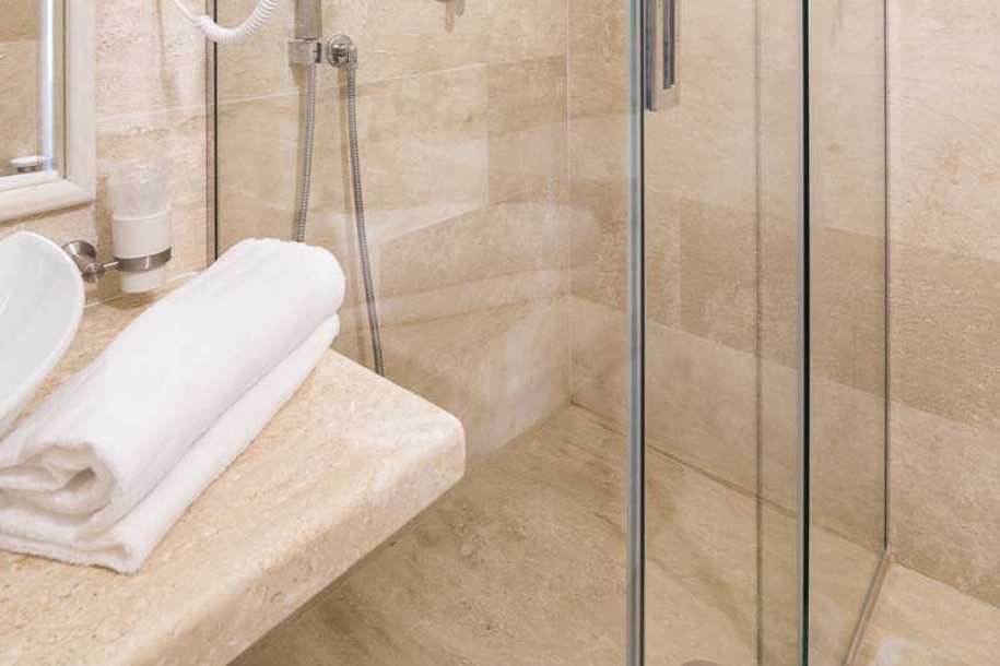 Elegante bagno con doccia in vetro e pareti in pietra chiara.